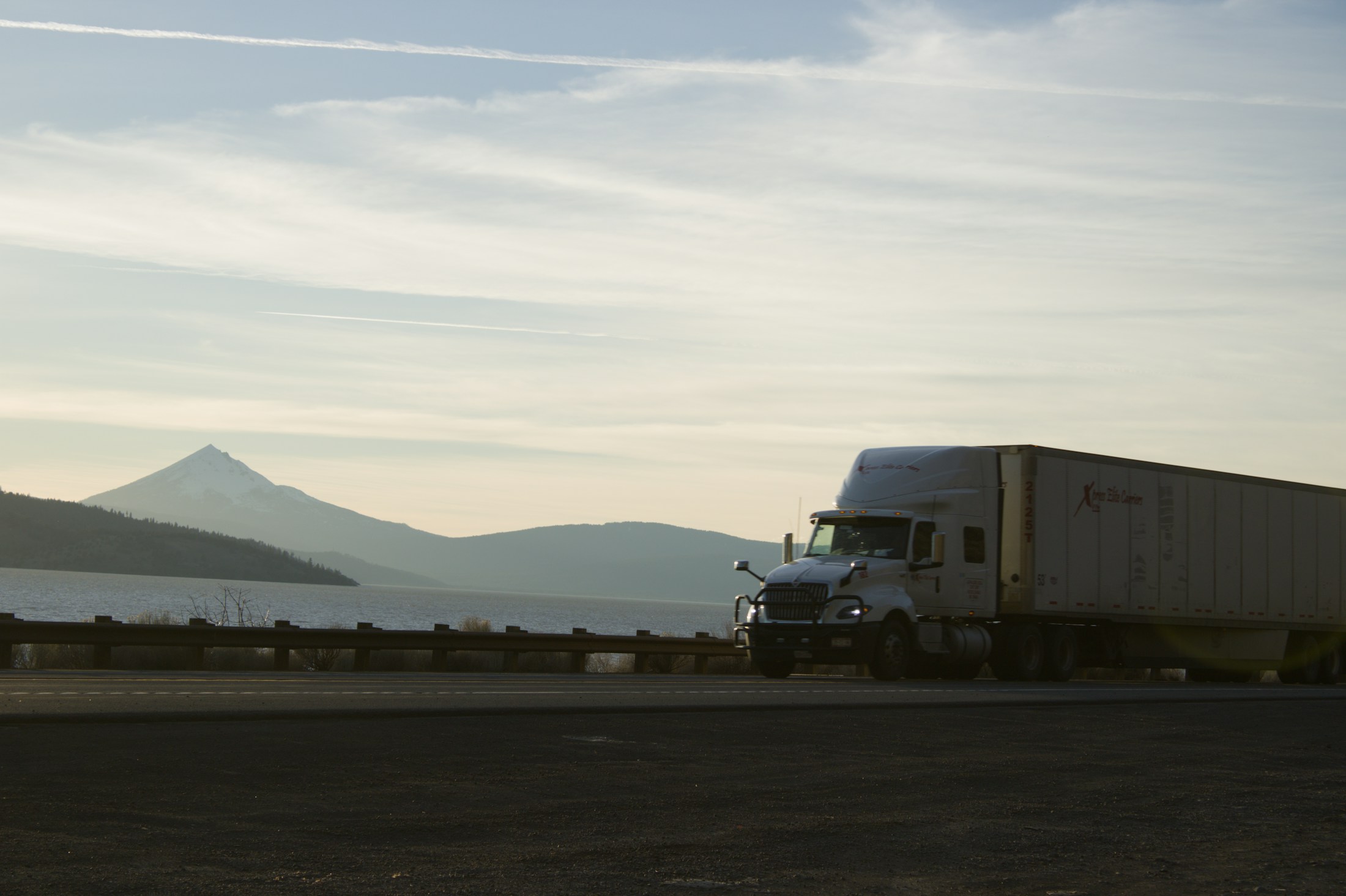 Semi truck traveling on a highway alongside a mountain lake